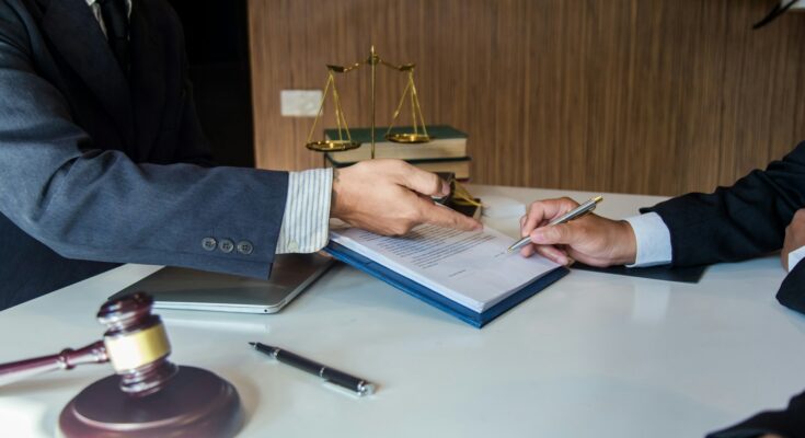 Client consulting with a legal professional, reviewing and signing important documents in an office setting, symbolized by a gavel and scales of justice in the background