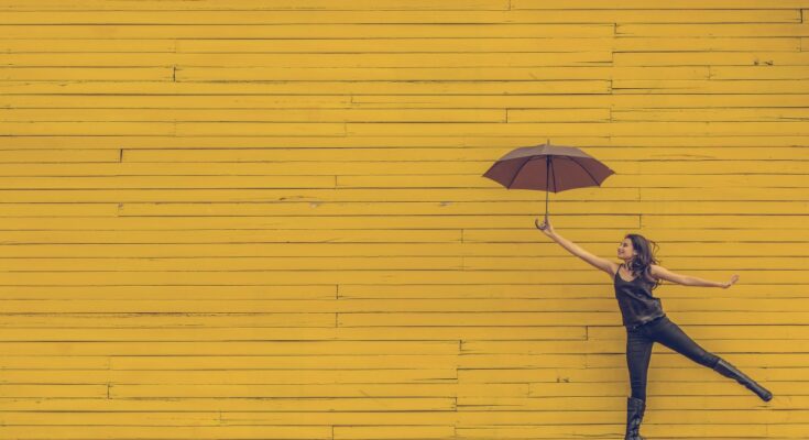 Woman holding a printed umbrella while smiling against a bright yellow wall.