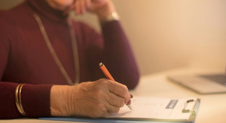Elderly woman writing on a clipboard while reviewing costs to contest a will in the UK